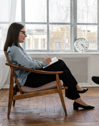 kobieta psycholożka z zeszytem na kolanach siedząca w fotelu pod oknem